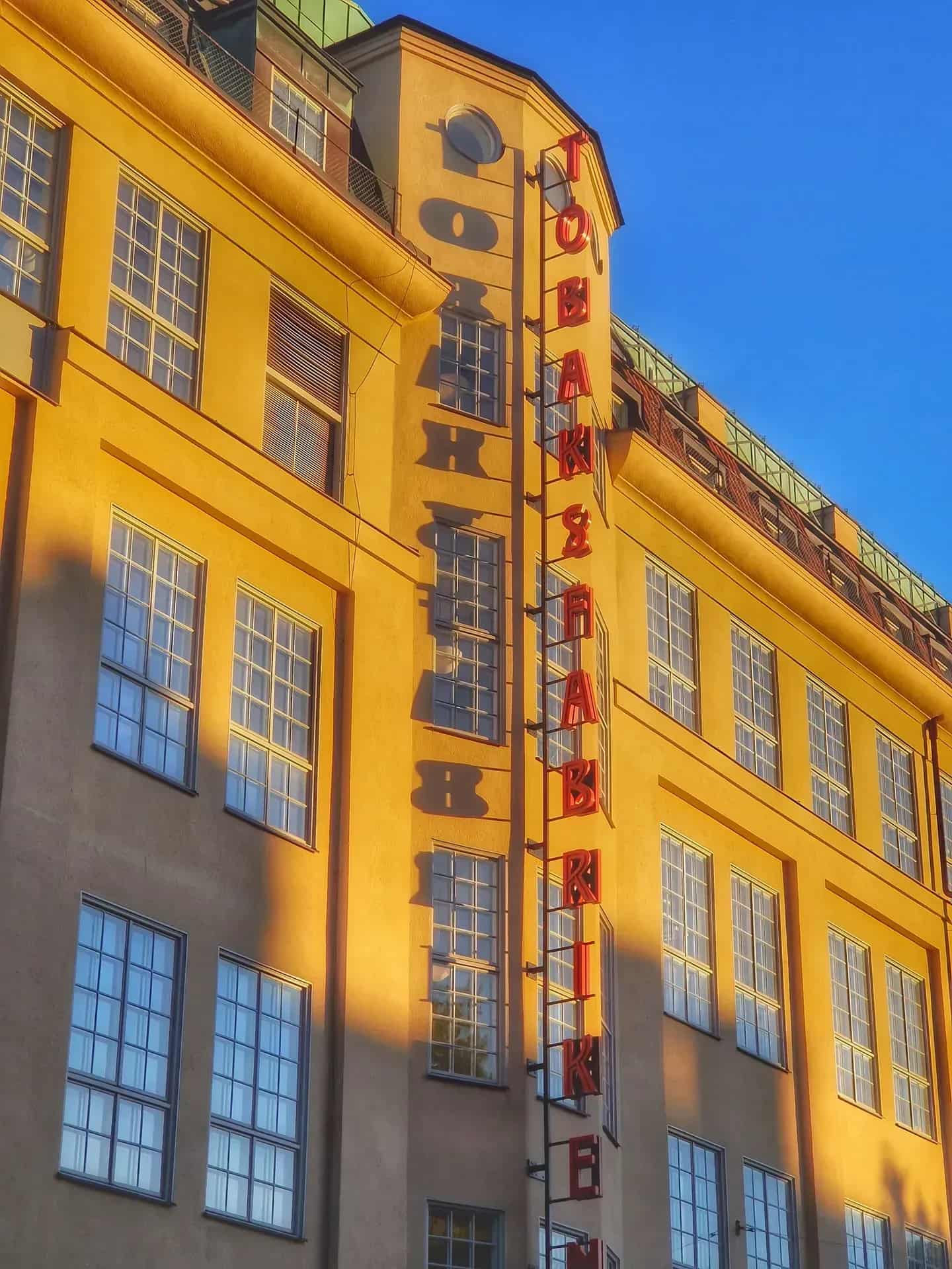 Facade of yellow house with many windows. Vertical sign with red letters: "Tobaksfabriken"