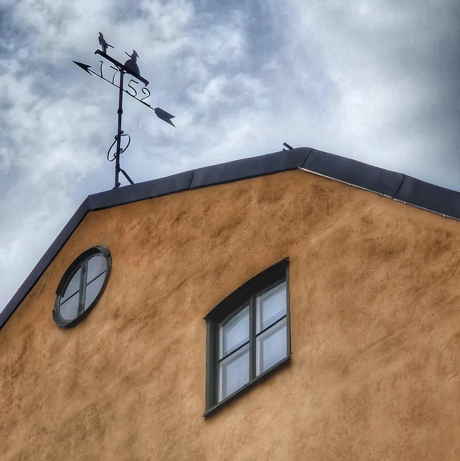 Gable with two windows, weather vane with the year 1752 and two silhouettes. Cloudy sky