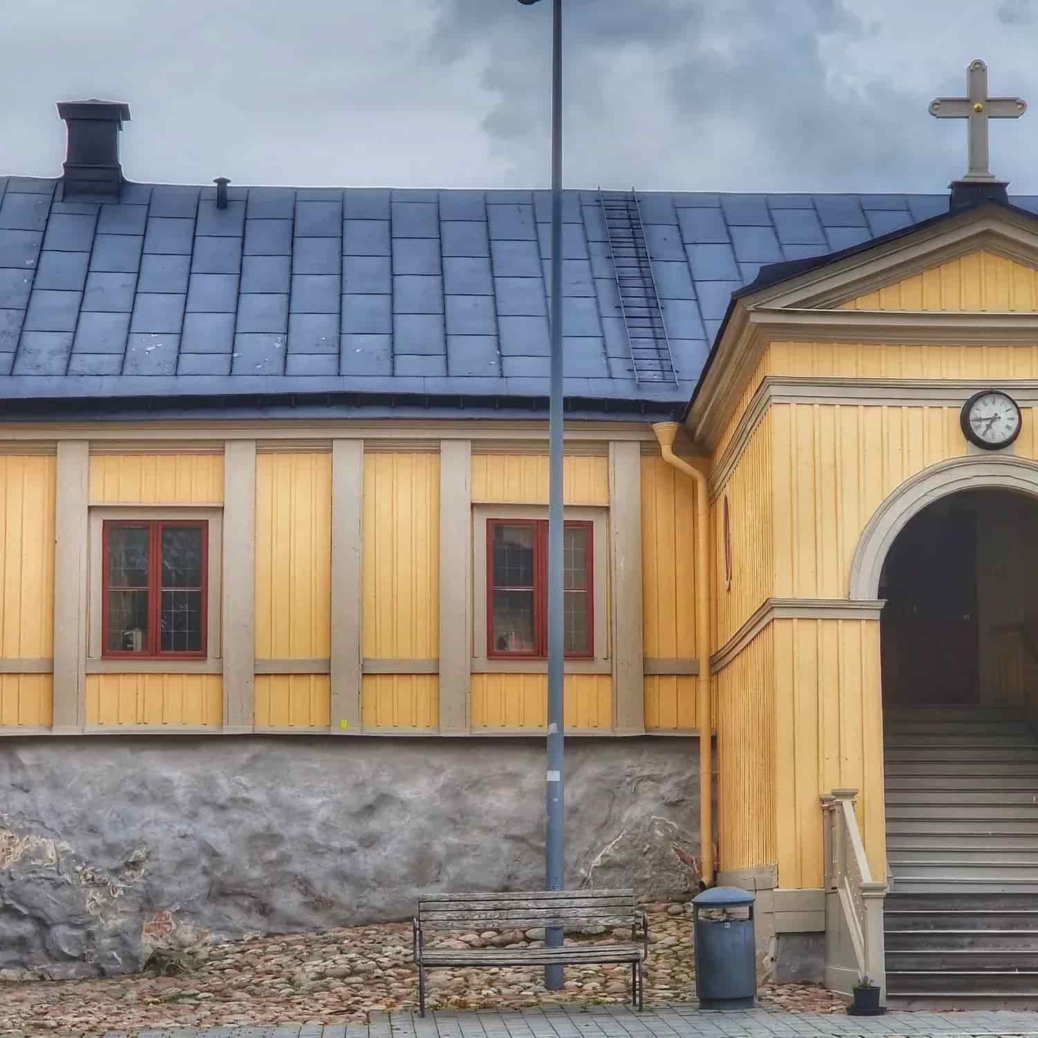 Gul byggnad med blått tegeltak, kors, stege, bänk och trappa