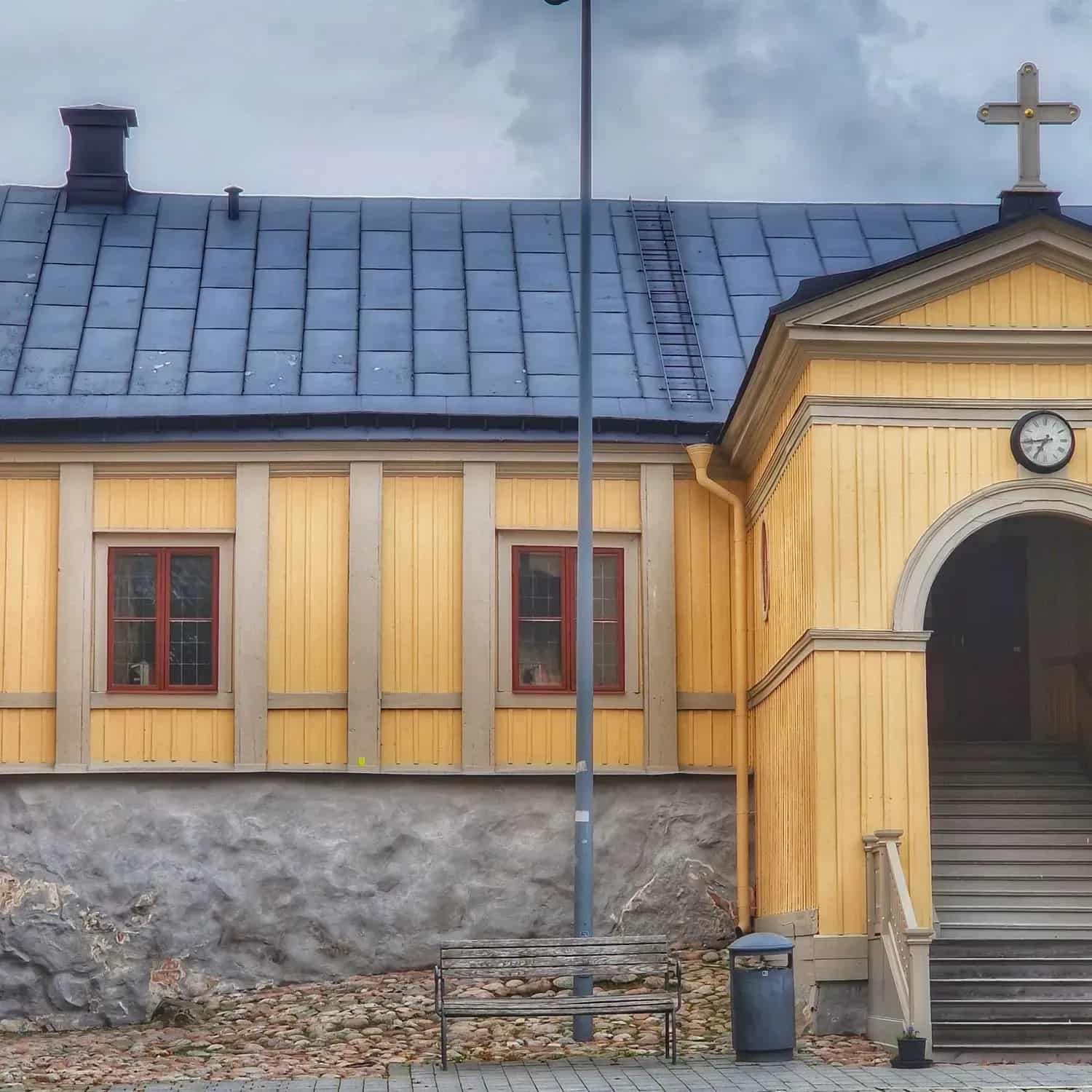 Yellow building with blue tile roof, cross, ladder, bench and stairs