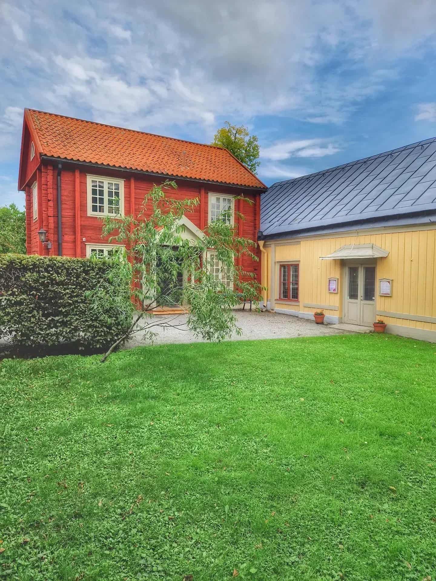 Rött trähus med tegeltak, gult trähus med plåttak, gräsmatta och blå himmel