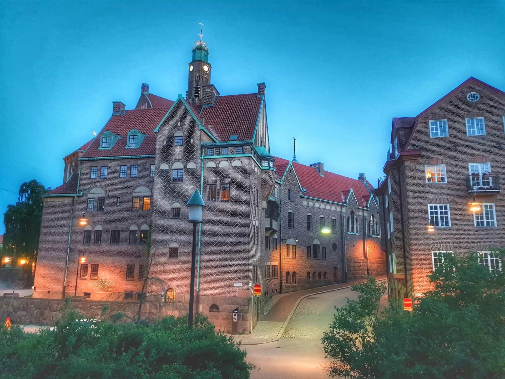 Tegelhus och en kullerstensgata i Lärkstaden Stockholm i skymningen med tända gatulyktor och ett klocktorn