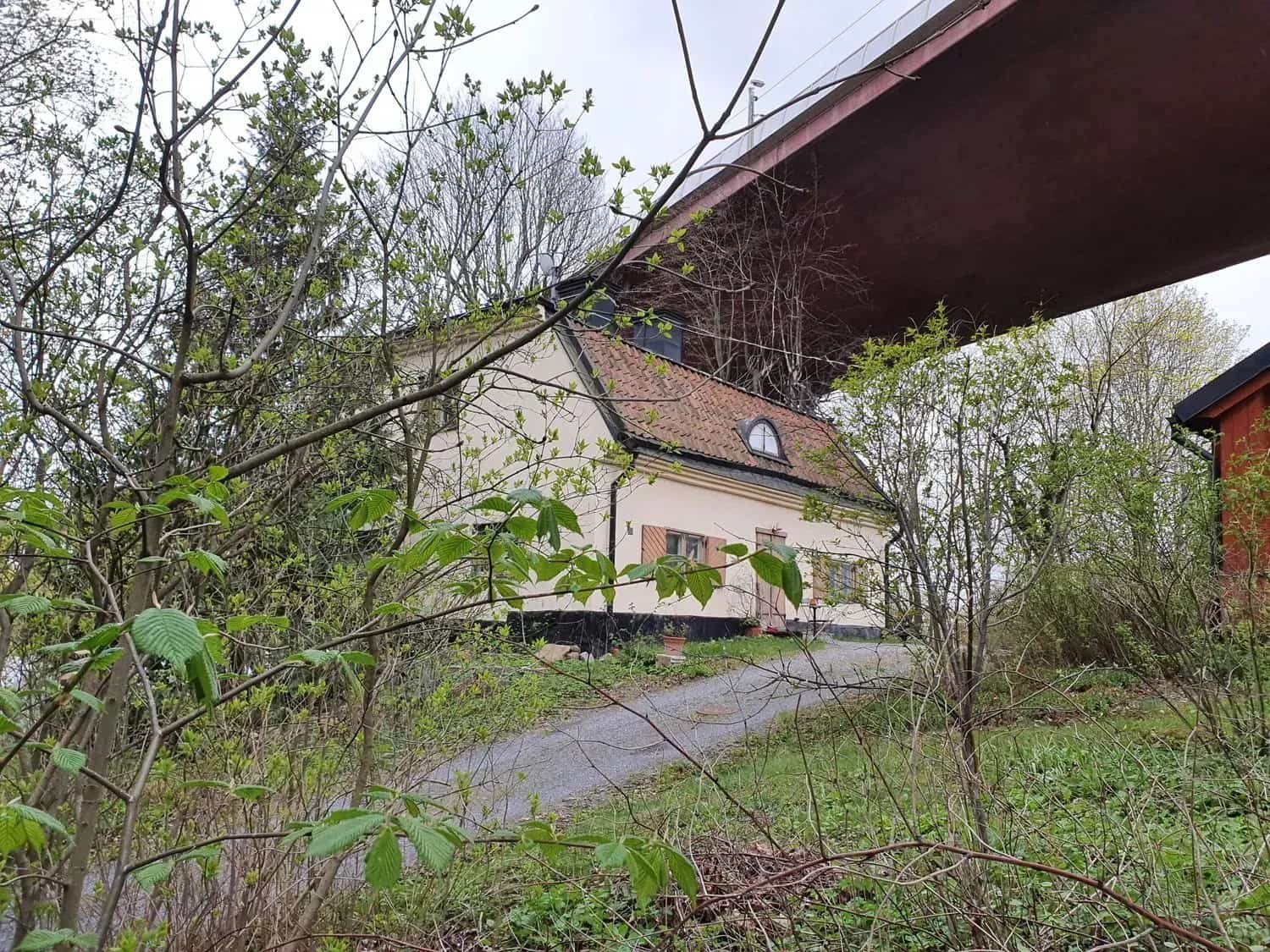 House with a red roof under a bridge. Bushes in the foreground
