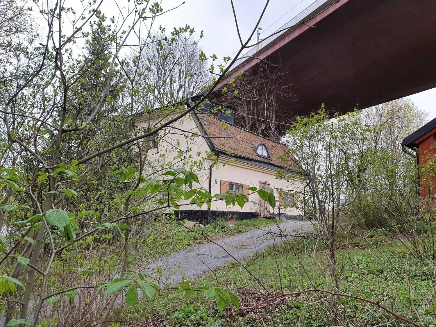 House with a red roof under a bridge. Bushes in the foreground