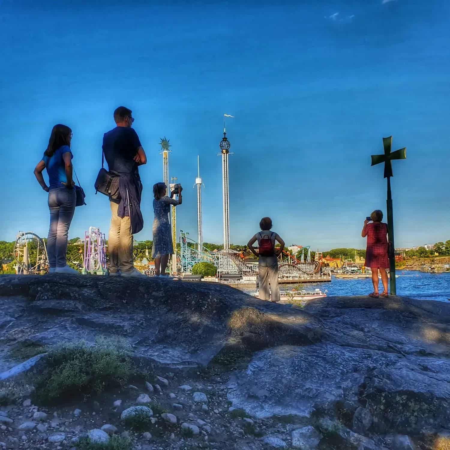 People on a cliff overlooking a funfair and water