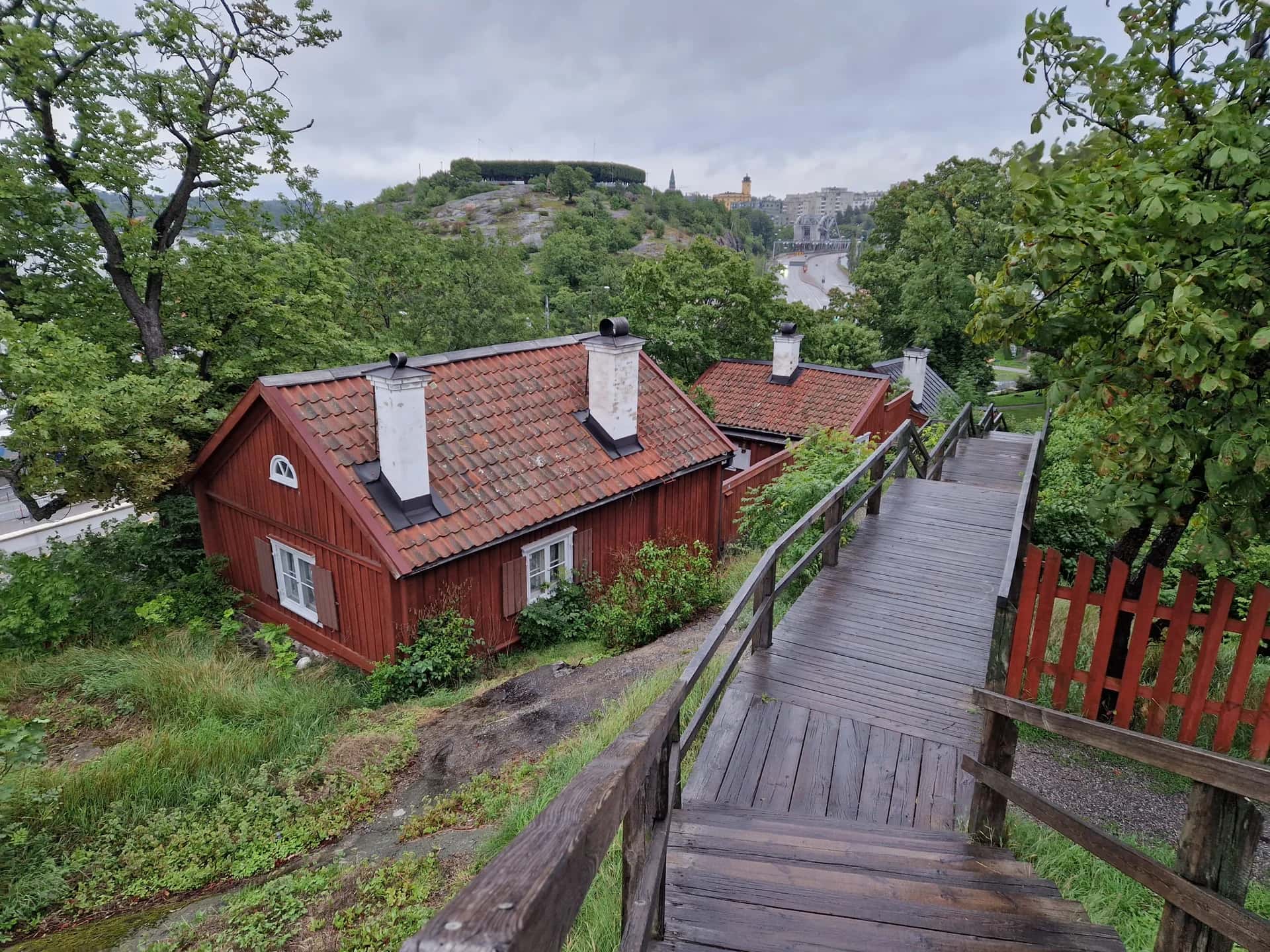 Röda hus och trätrappa i grönska med stad och vatten i bakgrunden, en klassisk vy för Stadsvandring Stockholm