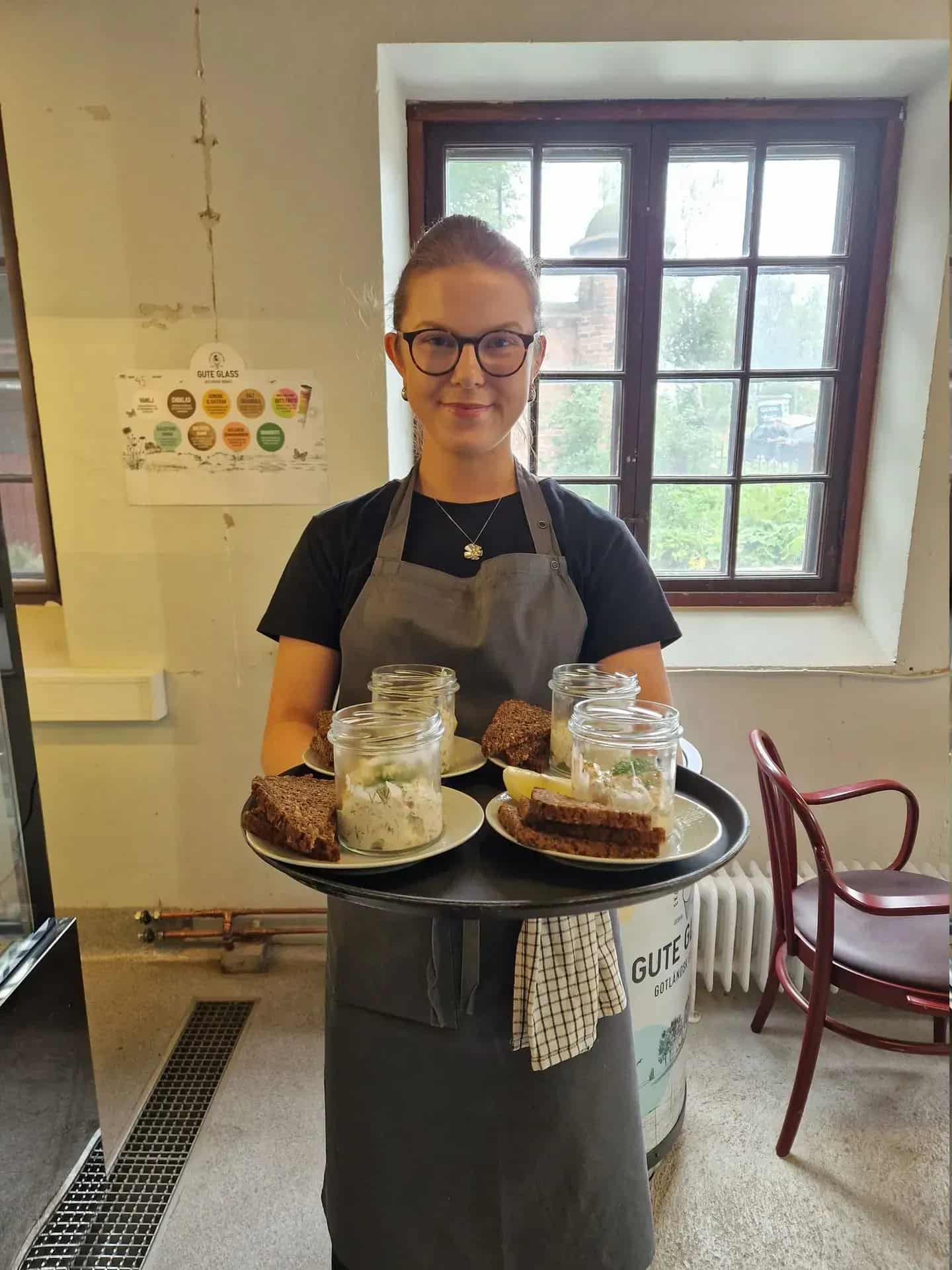 Waitress carries tray with sandwiches and glass jars. Window in the background