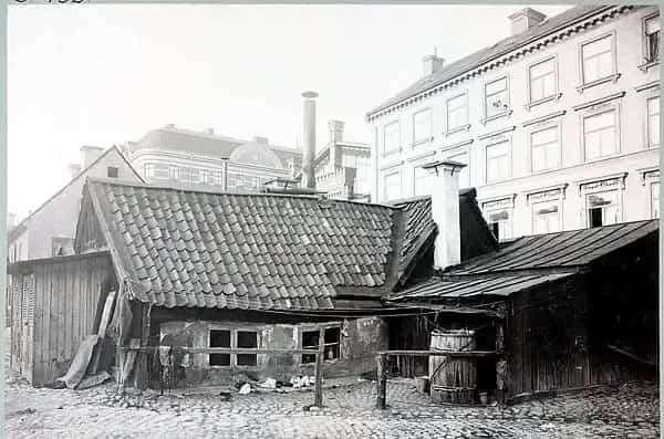 Older building with tiled roof, visible courtyard with cobblestones. Houses in the background