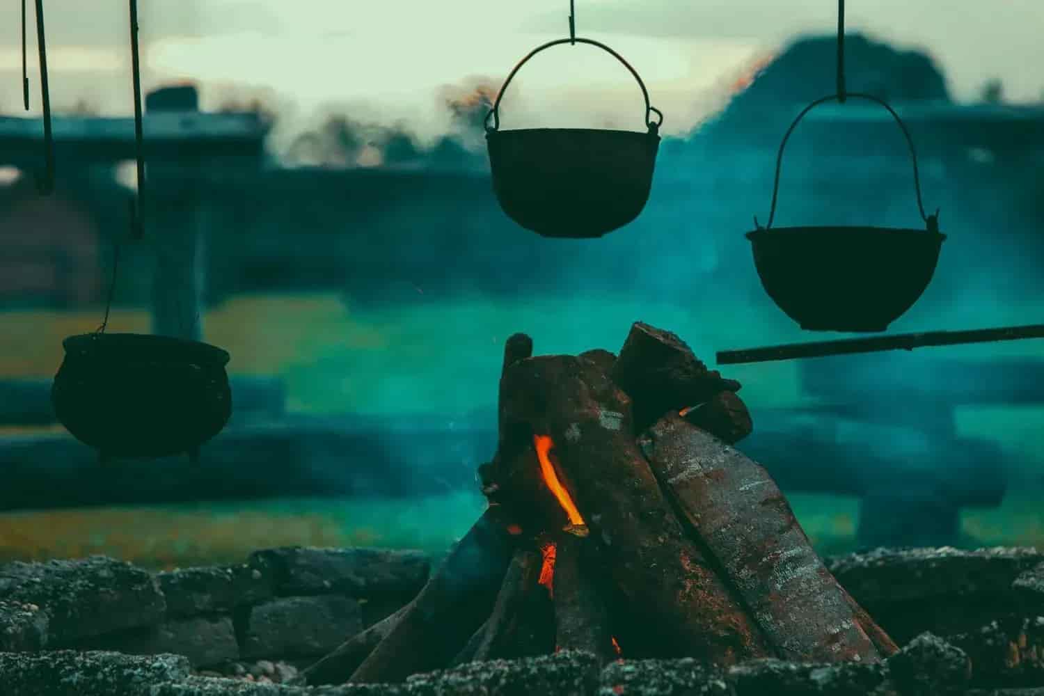 Fire with wood in a stone circle. Three black pots hang above. Smoke