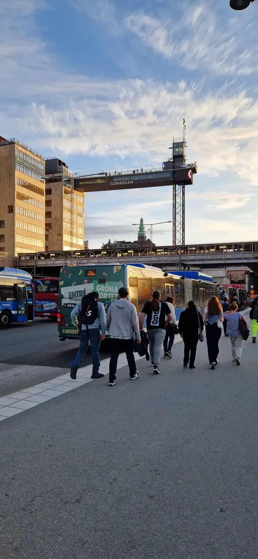 Pedestrians pass buses by a building with the sign Gondolen