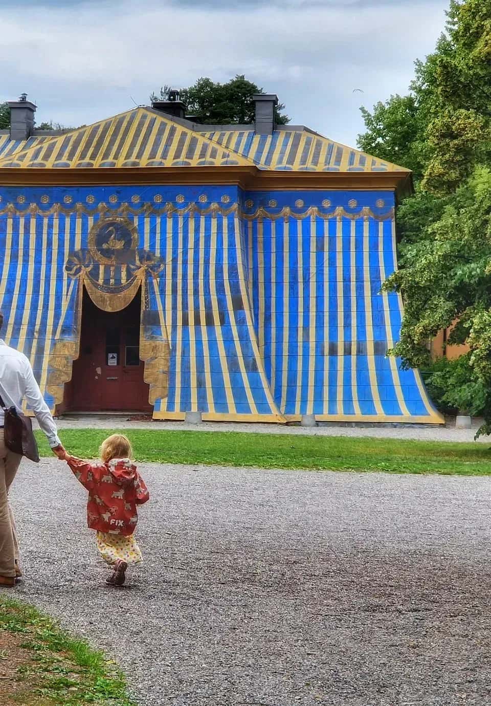 Man and child hand in hand in front of building painted as tent in blue and yellow