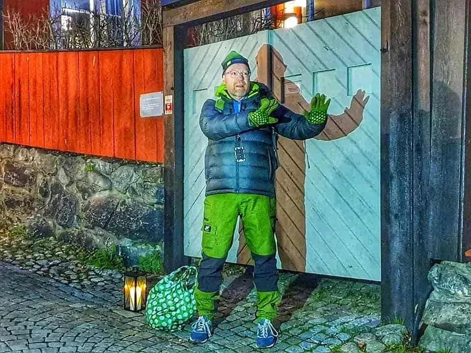 Man in green outfit in front of light blue door. Bag, lantern