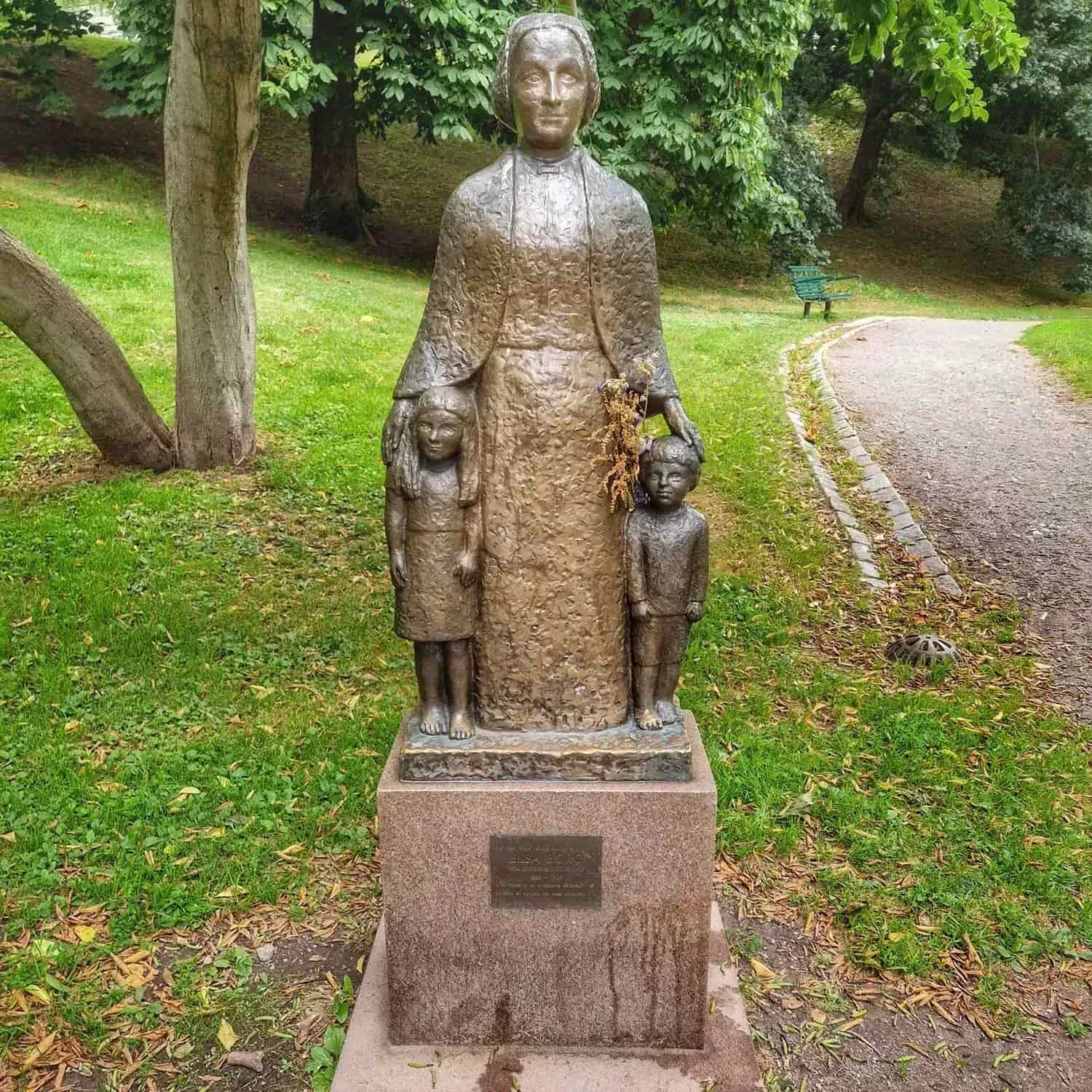 Bronsstaty: kvinna med två barn, på stensockel i park