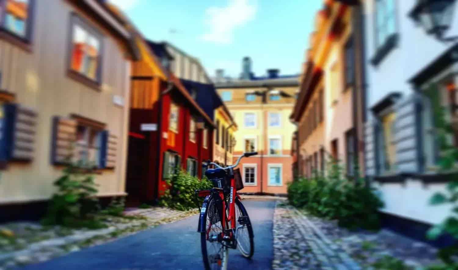 Röd cykel parkerad på kullerstensgata bland färgstarka trähus