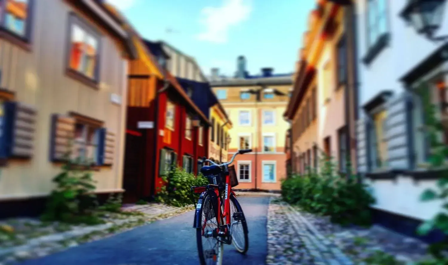 Röd cykel parkerad på kullerstensgata bland färgstarka trähus