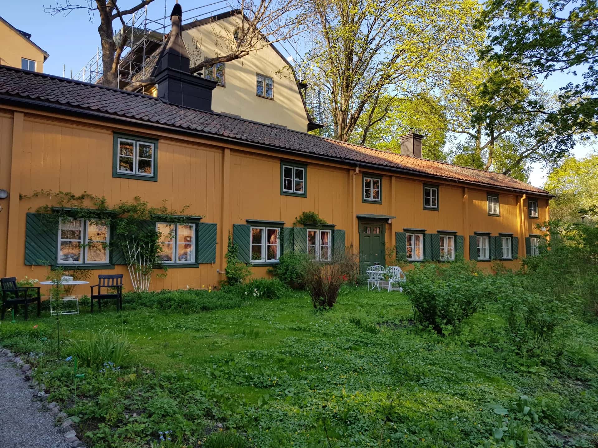 Gult trähus med gröna fönsterluckor och trädgård under en stadsvandring i Stockholm