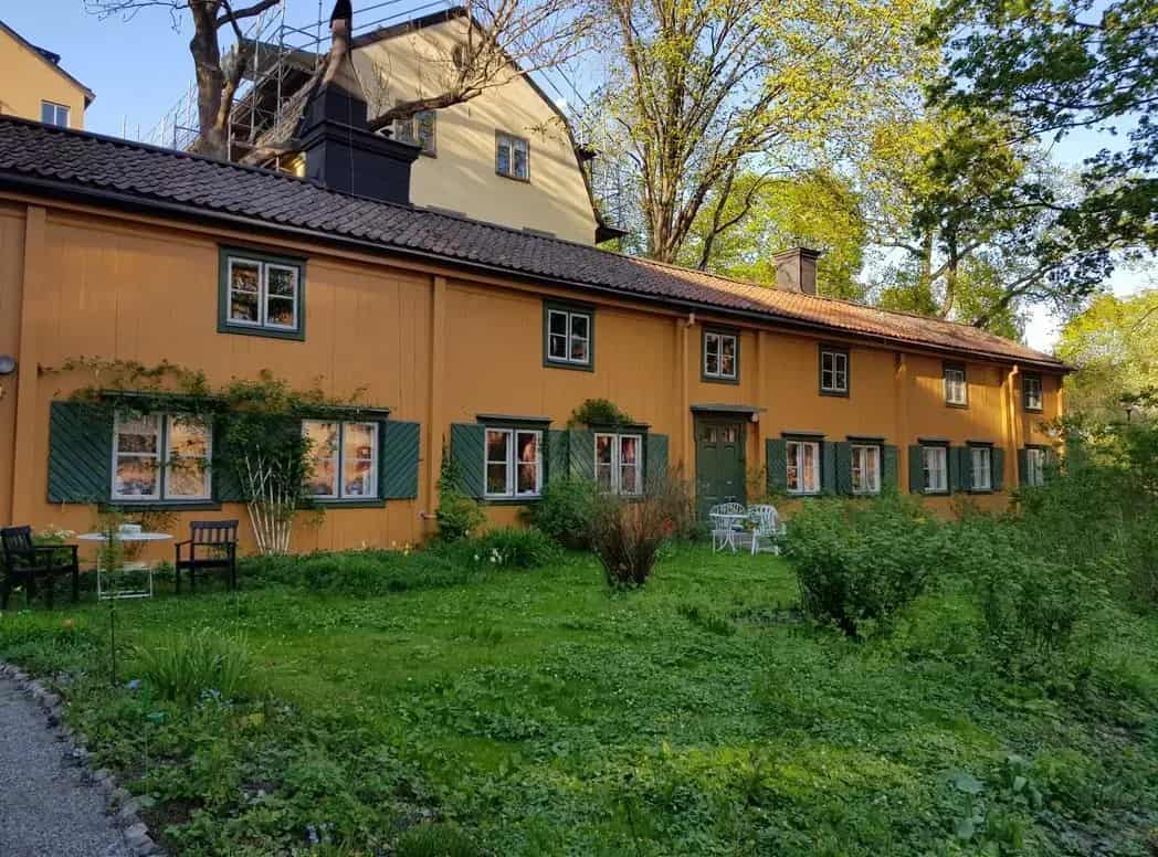 Low, yellow house with green door and green shutters. Grassy ground in front. Trees in the background