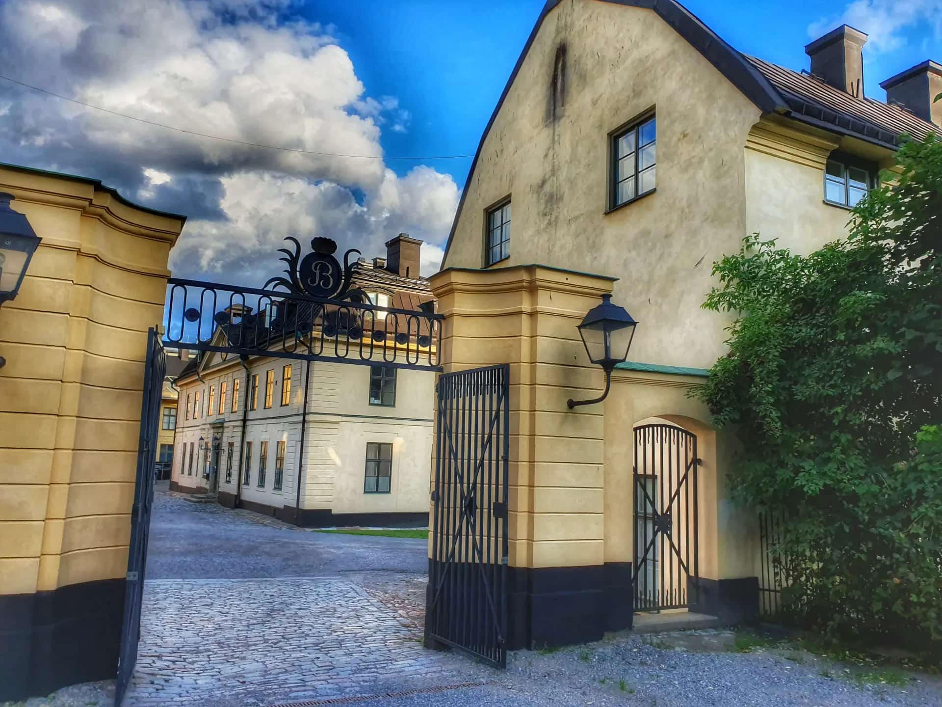 Gate opens to cobblestone street with bright buildings. Blue sky with clouds