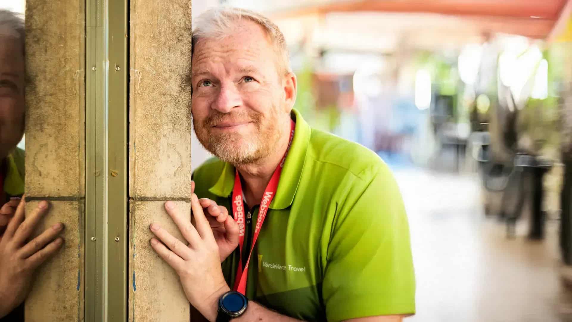 Man i grön tröja med rött band runt halsen, lutar mot vägg