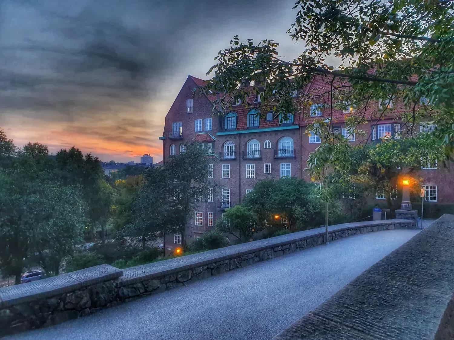 Asphalted walkway with stone obstacles, brick building and trees under a dramatic sky