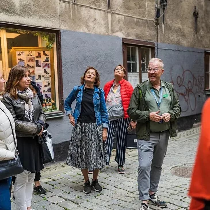 Grupp människor på kullerstensgata, några tittar uppåt. Butiksfönster med skor i bakgrunden