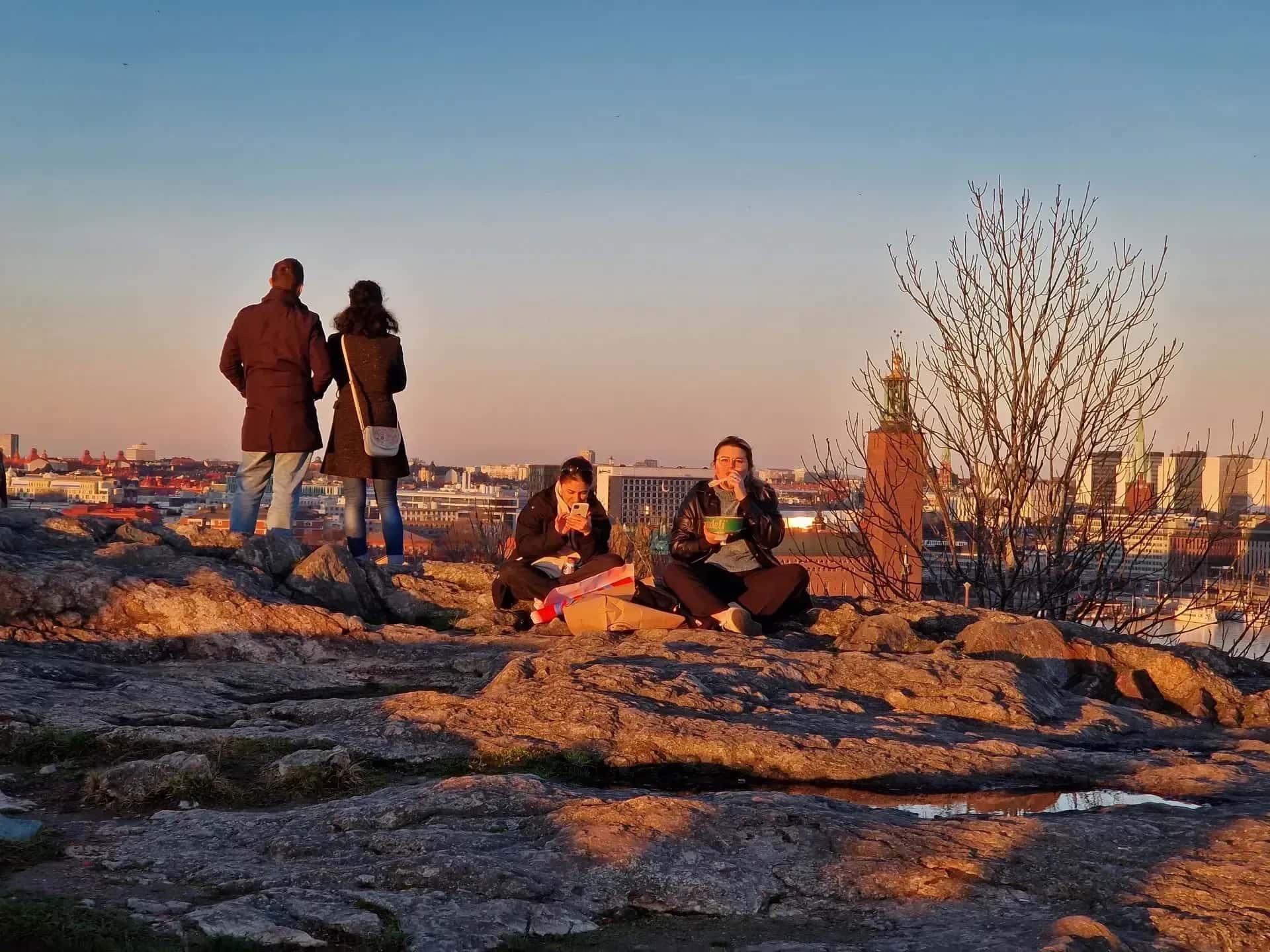 Folk sitter på klippor i solnedgång med Stockholm i bakgrunden