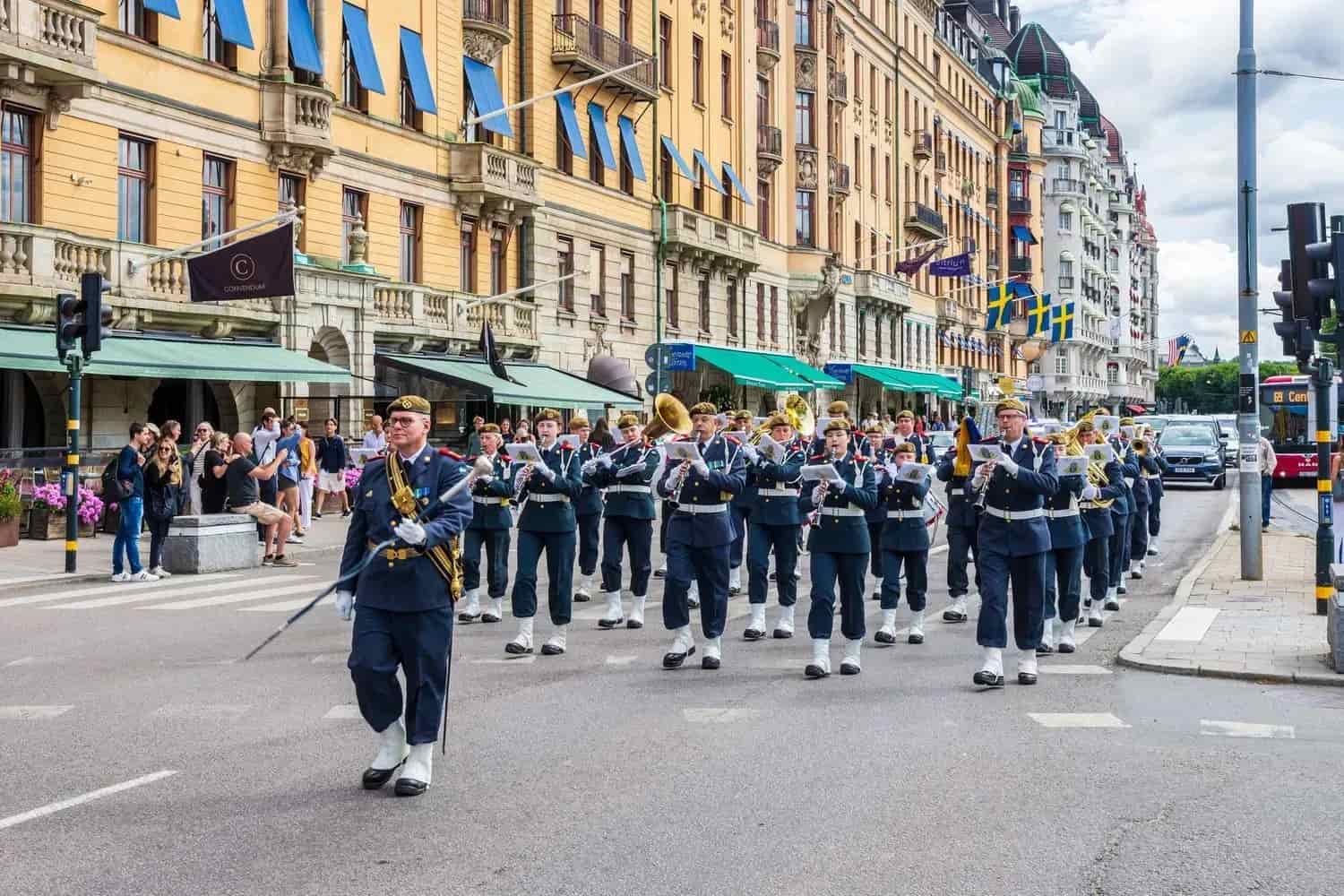 Marching band in uniform marching on street. Buildings in background