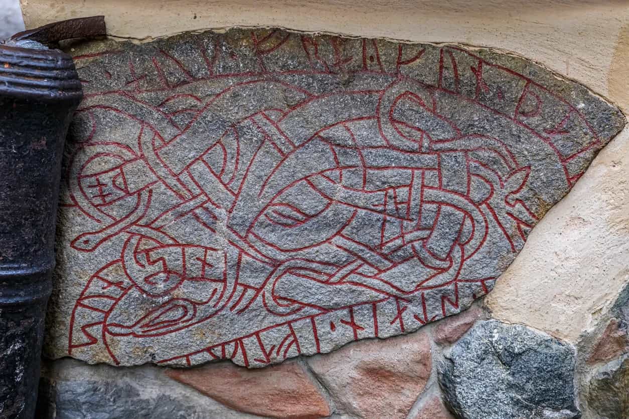 Grå sten med röda slingrande runliknande sniderier inmurad i en vägg. Arkitektur Gamla stan