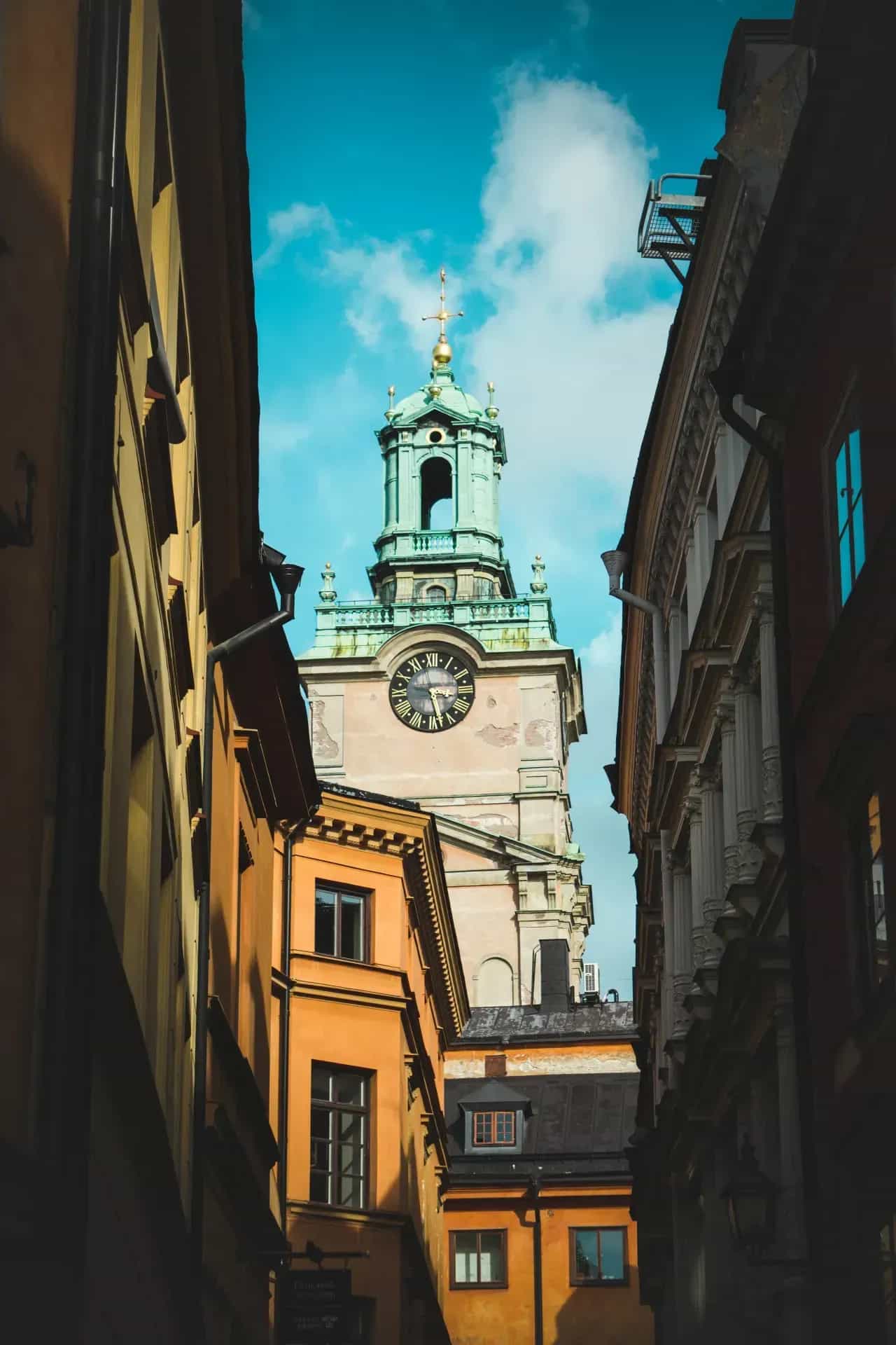 Kyrktorn med klocka och kors, sedd mellan byggnader i Gamla Stan