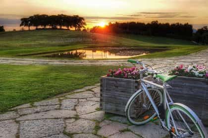 Silver colored bicycle by flower boxes. Lake, hill and sunset in the background