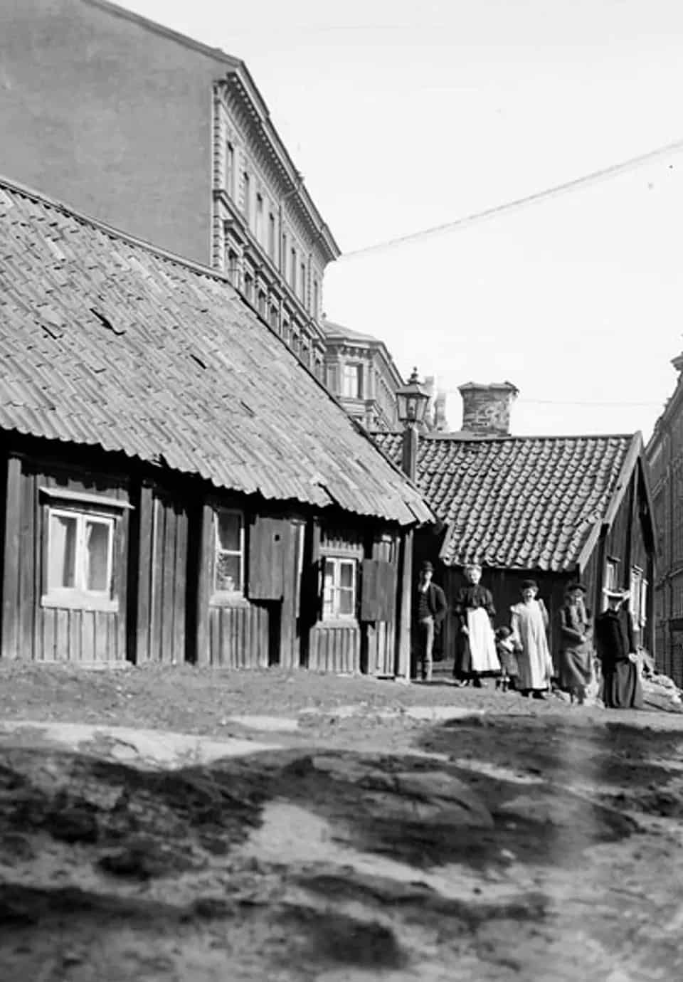 Black and white image of wooden houses, brick houses and a group of people