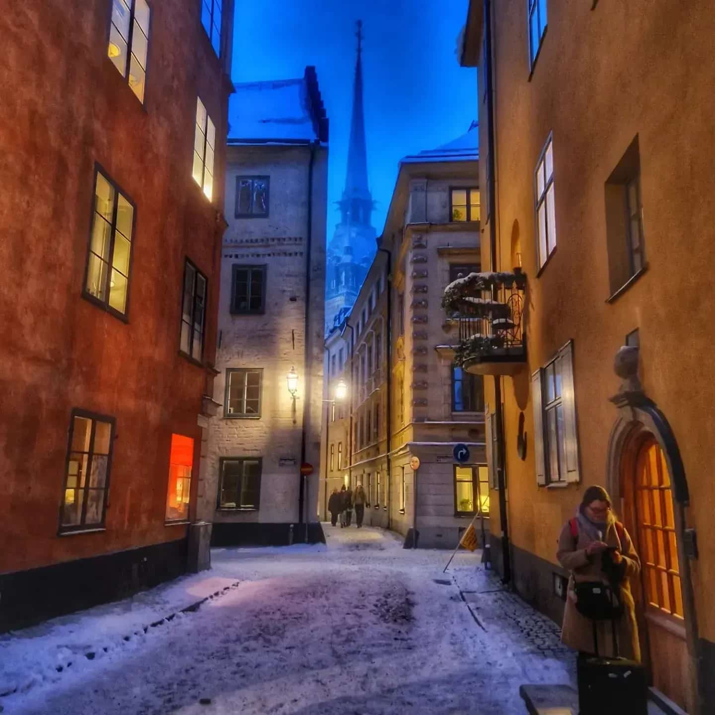 Street in the Old Town, Stockholm, with snow and a person with a suitcase. Church tower visible