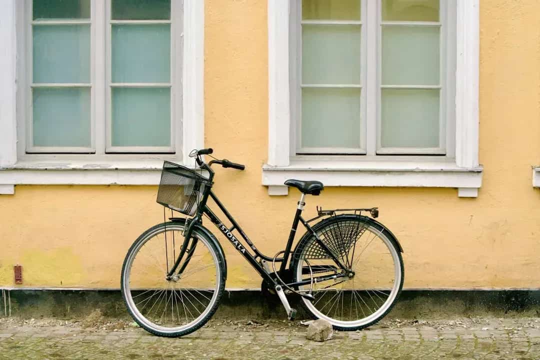 Svart cykel med korg mot gul vägg med vita fönster