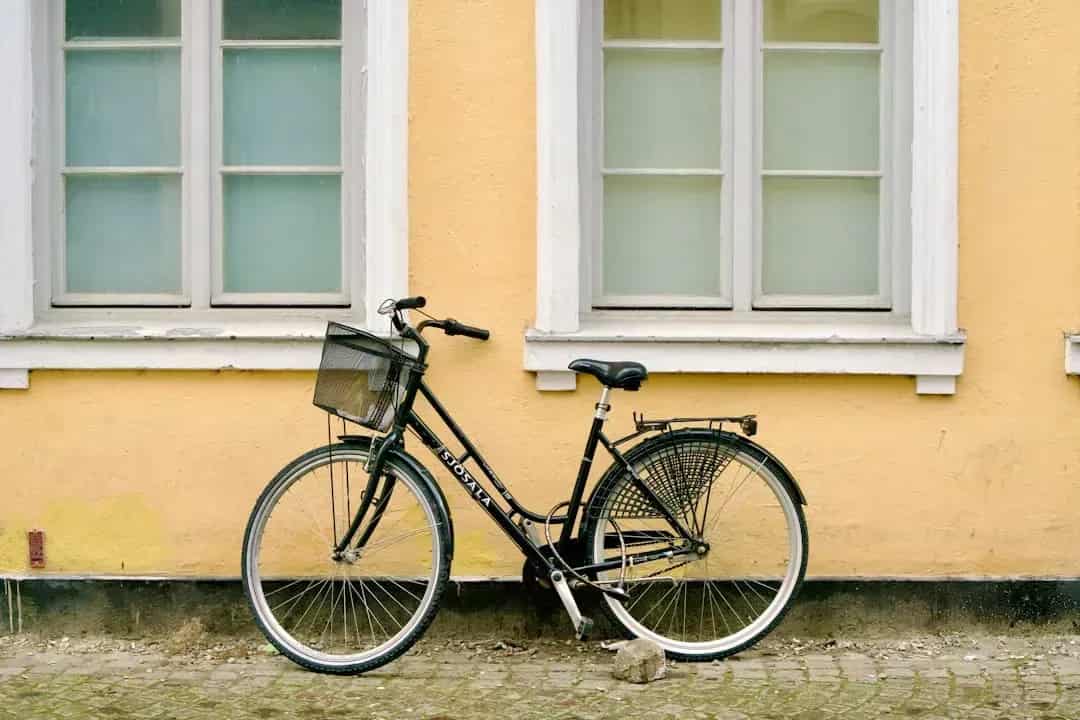 Svart cykel med korg mot gul vägg med vita fönster