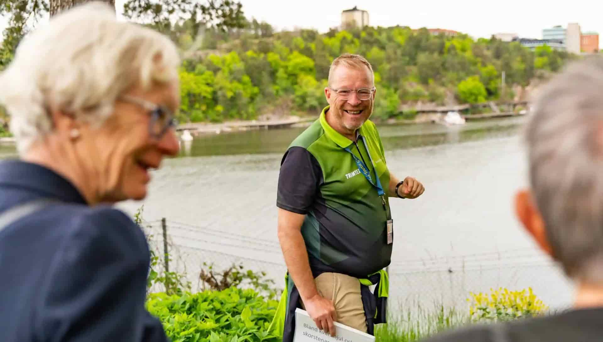 Man in green shirt, glasses and ID card smiles at spectators. Water in the background